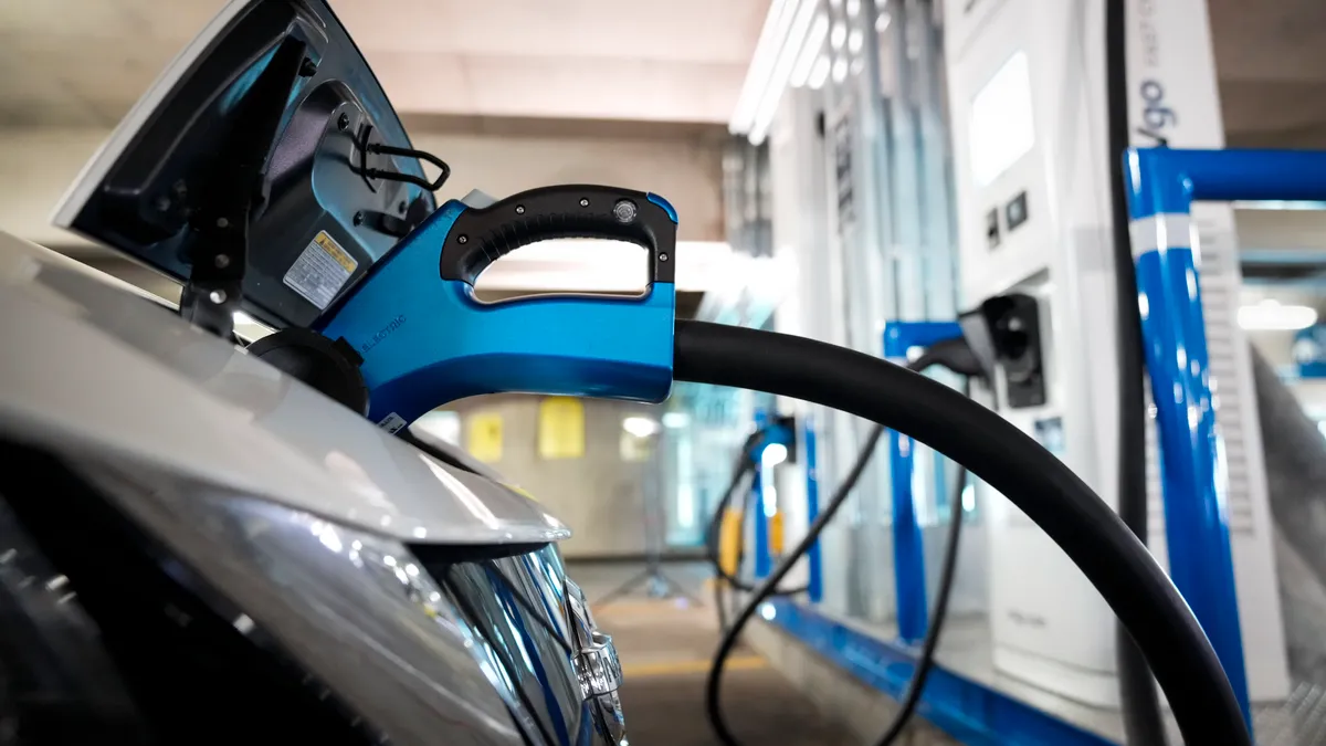 The front of a silver car is connected to an electric vehicle charger.