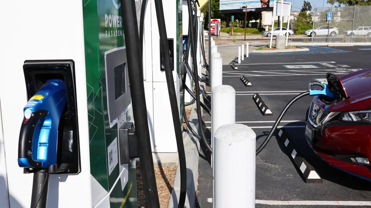 A row of electric vehicle chargers is seen from one end with a dark red vehicle parked and plugged in to the nearest charger.