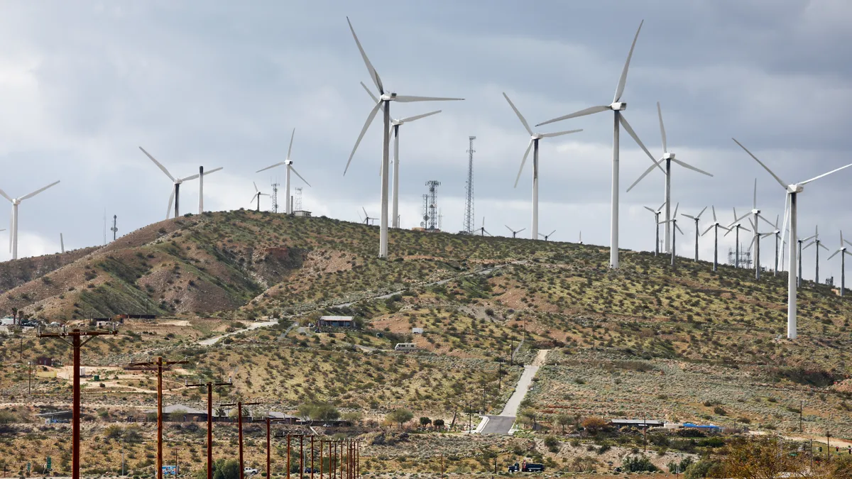 Wind turbines operate at a wind farm in Coachella Valley, as vehicles drive on a highway below.