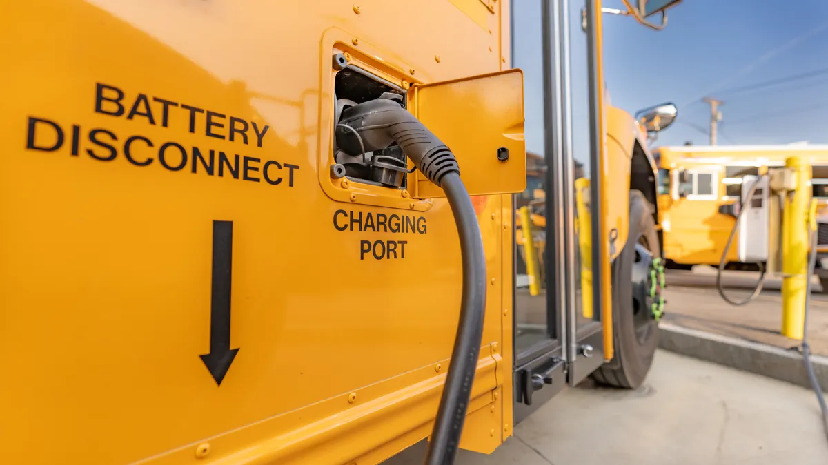 A yellow electric school bus is plugged in at a charging station.