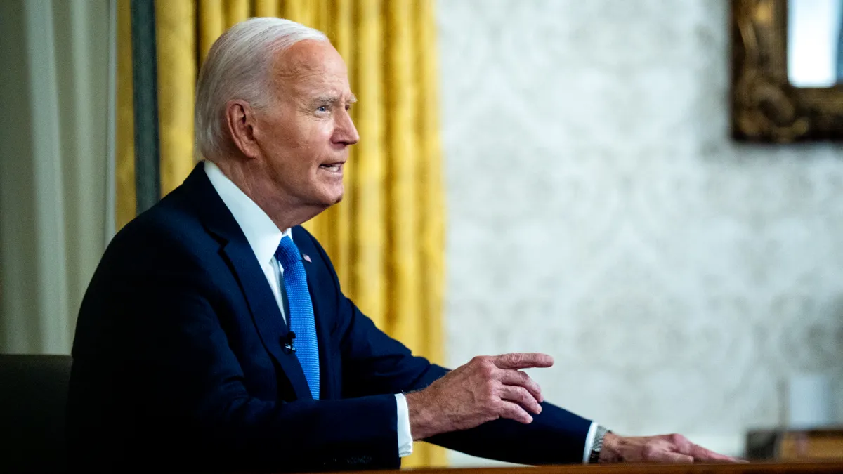 President Joe Biden sits at a desk to deliver an address.